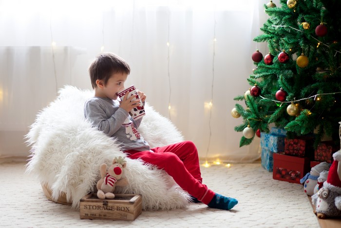 Boy drinking from mug by Christmas tree