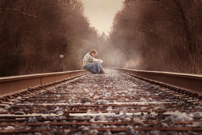 Man sitting on railroad tracks in a forest