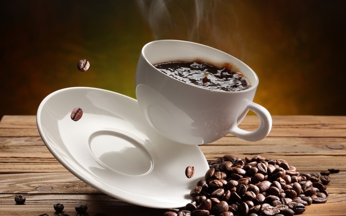 Steaming cup of coffee with beans and saucer