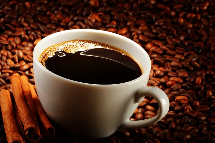 Coffee cup with cinnamon sticks on coffee beans