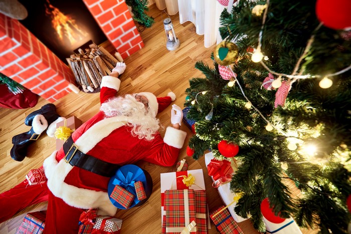 Santa Claus sleeping by Christmas tree and fireplace with gifts