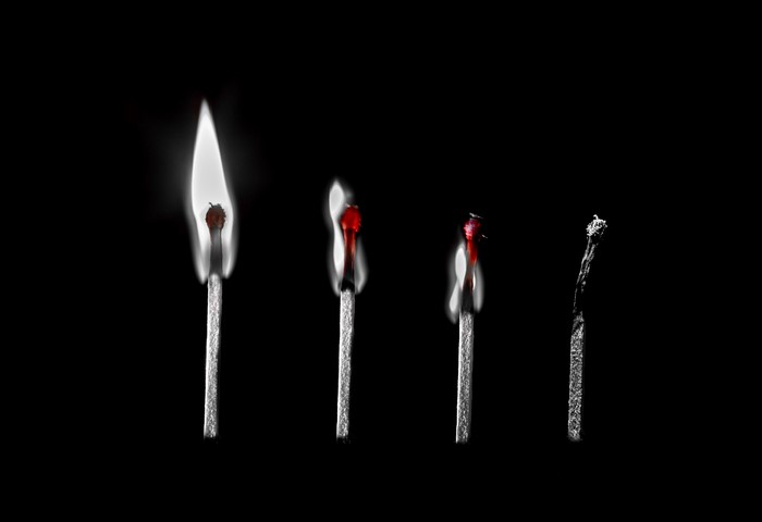 Four matches on a black background, one burning brightly