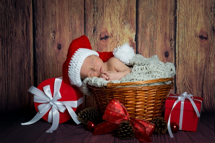 Baby in Santa hat sleeping in basket with Christmas gifts