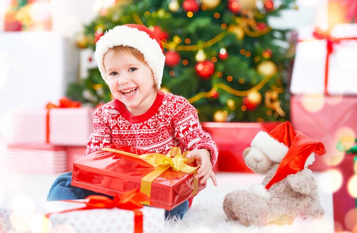 Little girl in Santa hat with Christmas gifts and teddy bear