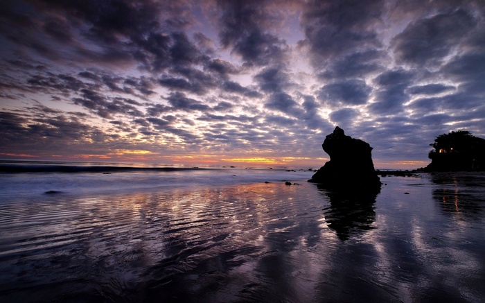 Sunset over the ocean with dramatic clouds and rock formations