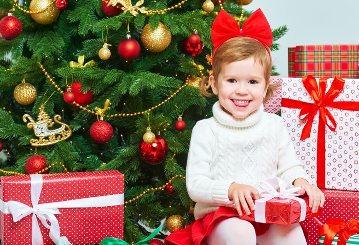 Little girl with red bow and gifts by Christmas tree