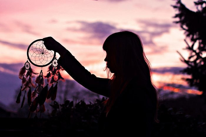 Silhouette of a person holding a dreamcatcher at sunset