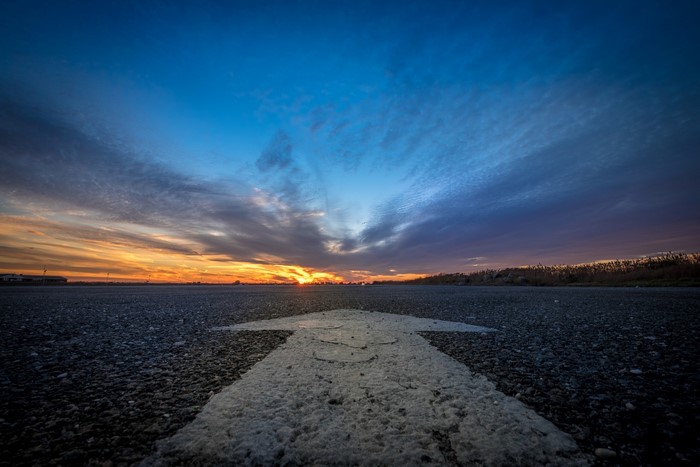 Arrow on asphalt road at sunset
