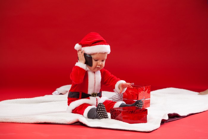 Baby in Santa costume talking on phone with gifts