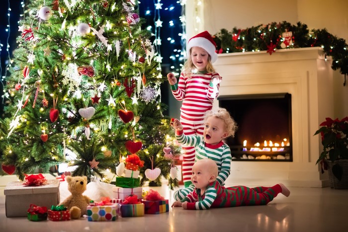 Children in pajamas by a Christmas tree and fireplace