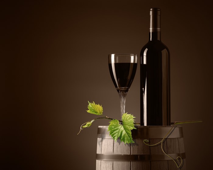 Wine bottle and glass on a barrel with grape leaves