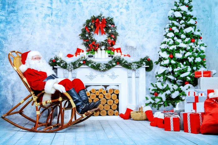 Santa Claus relaxing in a rocking chair by a fireplace and Christmas tree