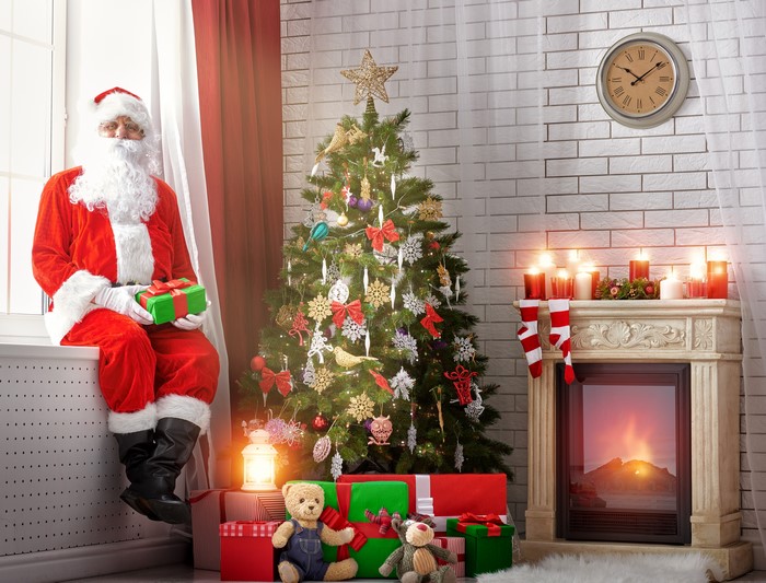 Santa Claus with Gifts by Christmas Tree and Fireplace