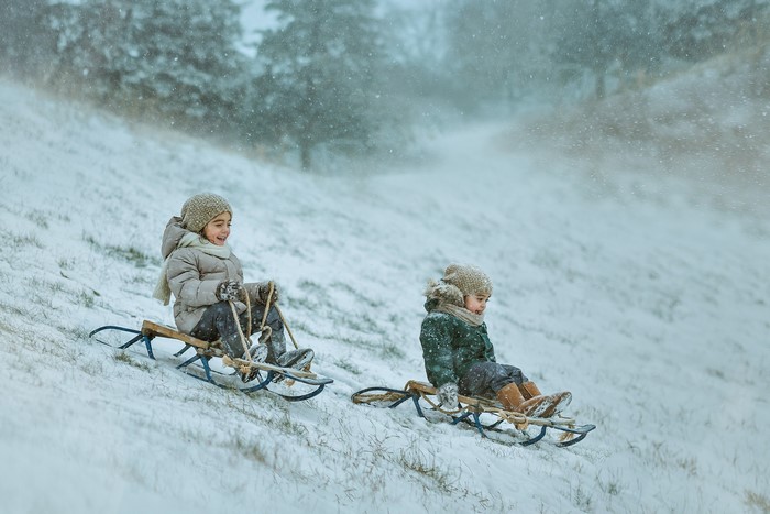 Two children sledding down a snowy hill