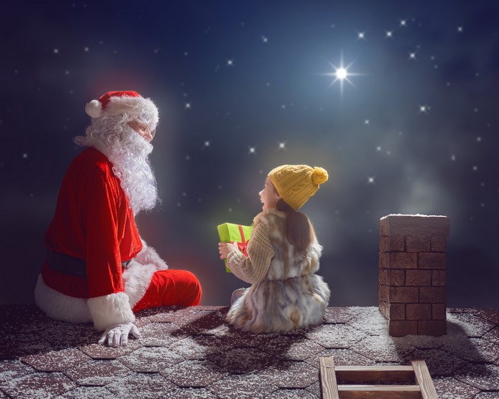 Santa Claus giving a gift to a girl on a snowy roof at night