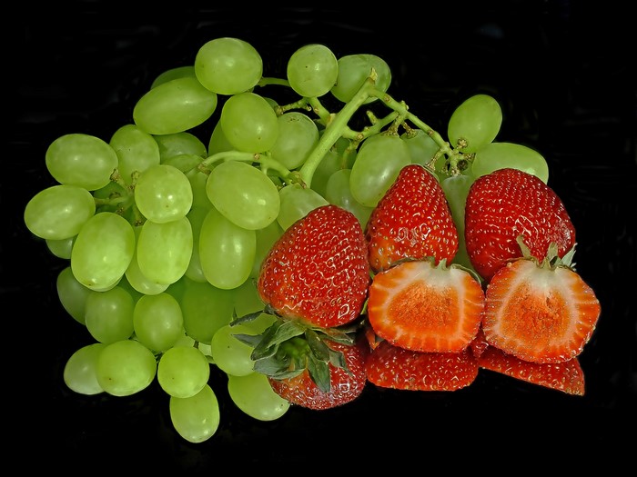Green grapes and strawberries on a black background with reflection