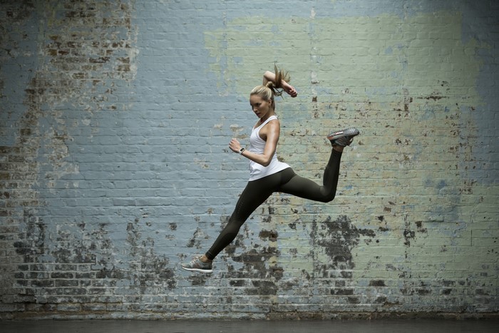Woman jumping in front of a brick wall