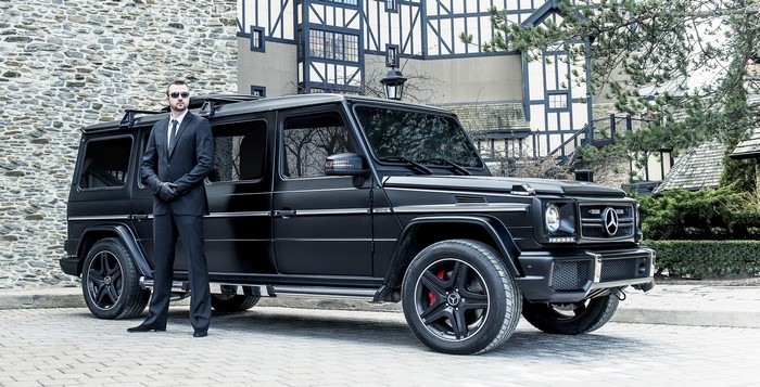 Man in suit standing next to black Mercedes-Benz G-Class
