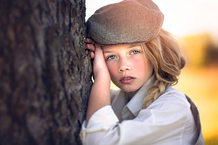 Girl in cap leaning on tree trunk