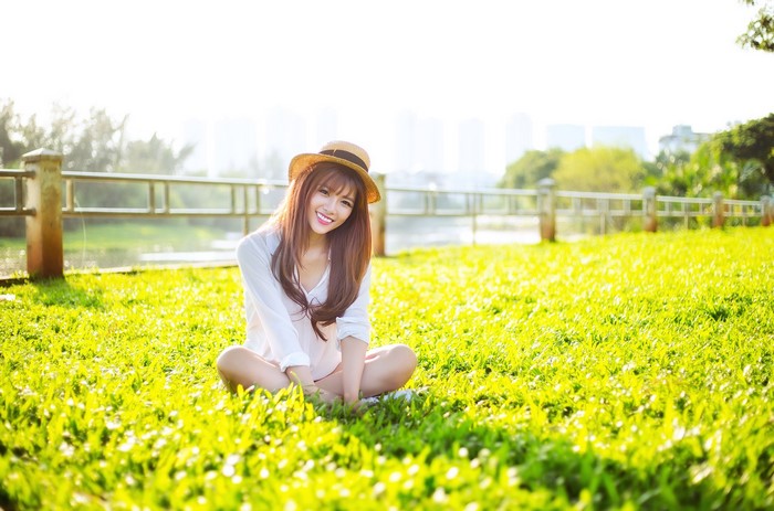 Asian woman with brown hair wearing a hat sitting on grass