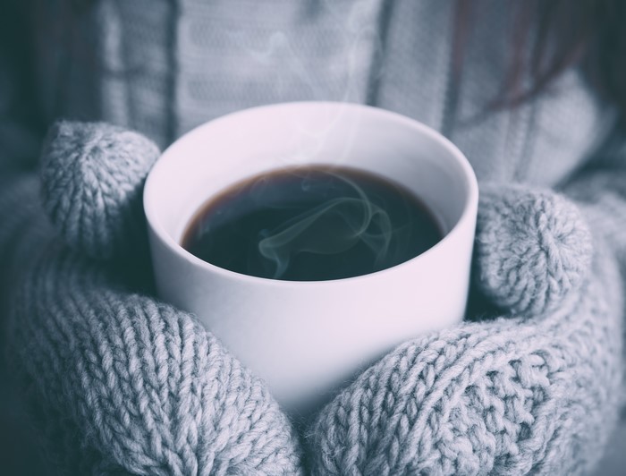 Cup of coffee with steam in mittens