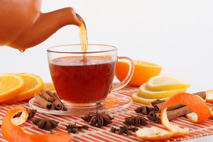 Tea being poured into a cup with oranges, lemons, cinnamon, and star anise