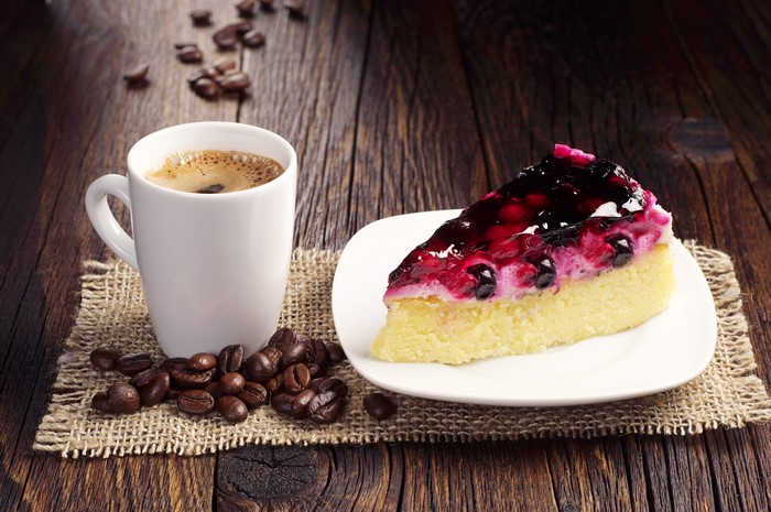 Coffee cup and berry cheesecake slice on wood