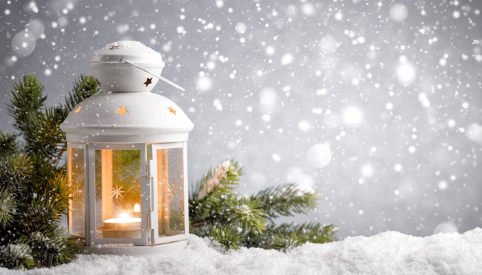 White lantern with candle in snow and pine branches
