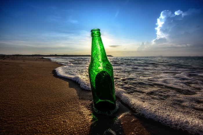 Green bottle on a beach with waves