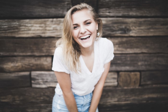 Young woman laughing in front of wooden wall