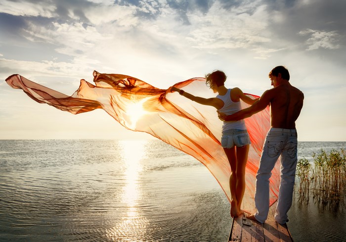Couple with flowing fabric at sunset over water