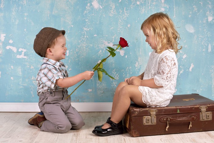 Boy giving a rose to a girl with a suitcase
