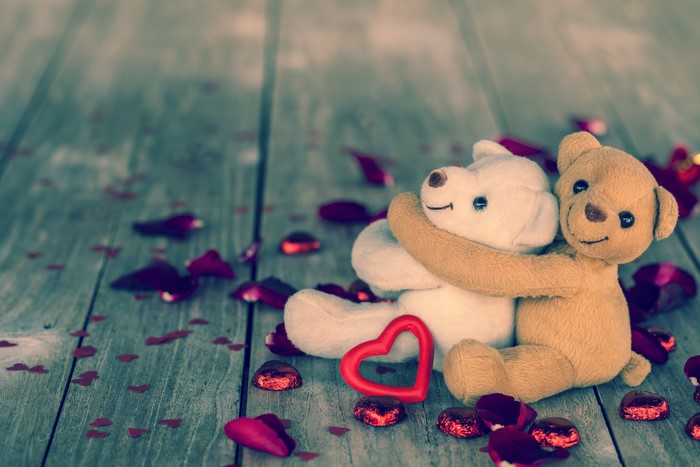 Two teddy bears hugging with rose petals and hearts
