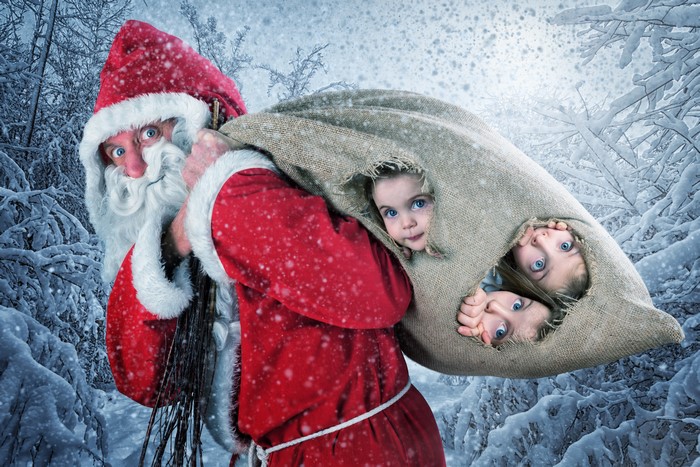 Santa Claus carrying a sack with children in a snowy forest