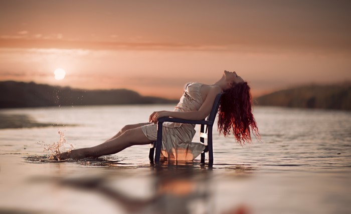 Redhead girl sitting in a chair in water at sunset