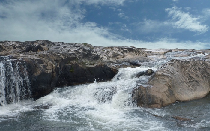 Rocky waterfall with turbulent water and cloudy sky