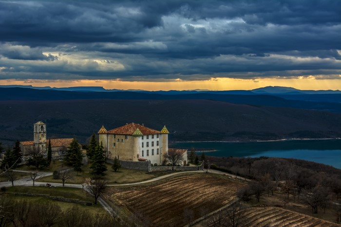 Chateau d'Aiguines and church overlooking a lake at sunset