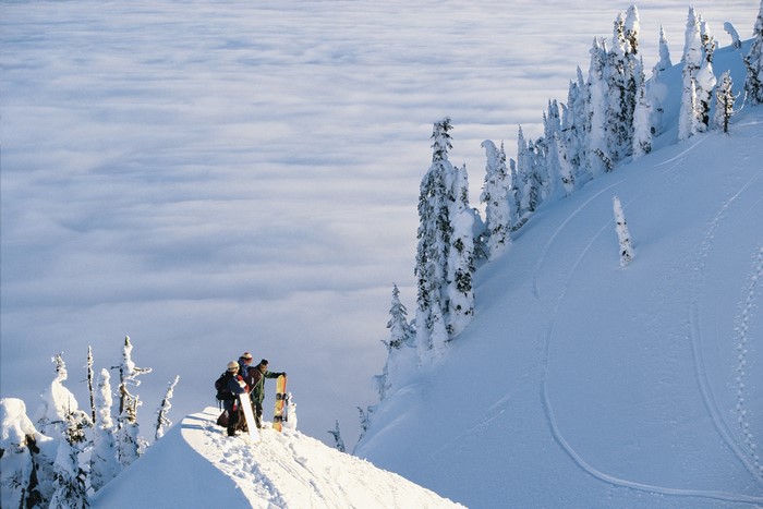 Snowboarders on a snowy mountain above clouds
