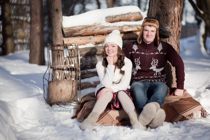 Couple sitting in the snow by a log pile