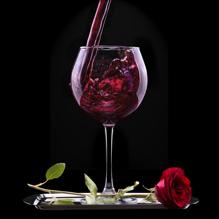 Red wine being poured into a glass with a rose