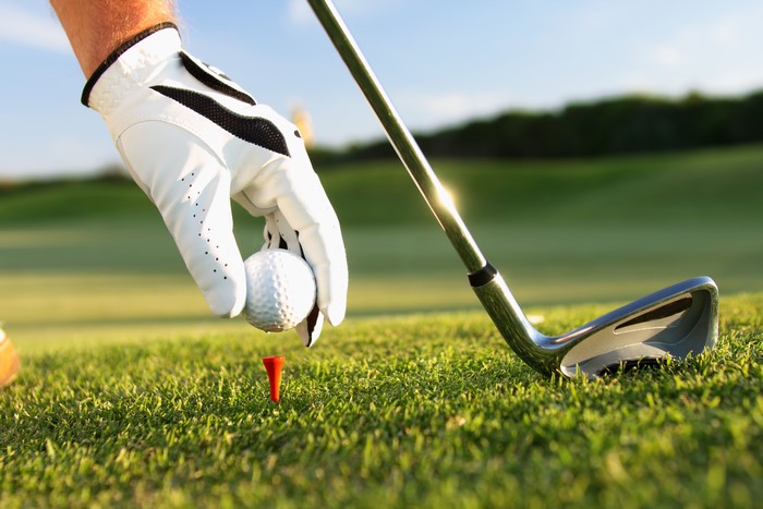 Golf glove placing ball on tee with club