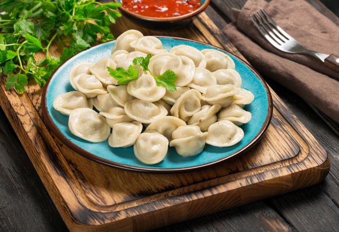 Pelmeni on a blue plate with sauce and parsley