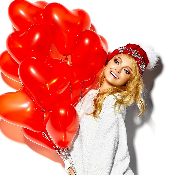 Blonde girl in winter hat holding red heart balloons