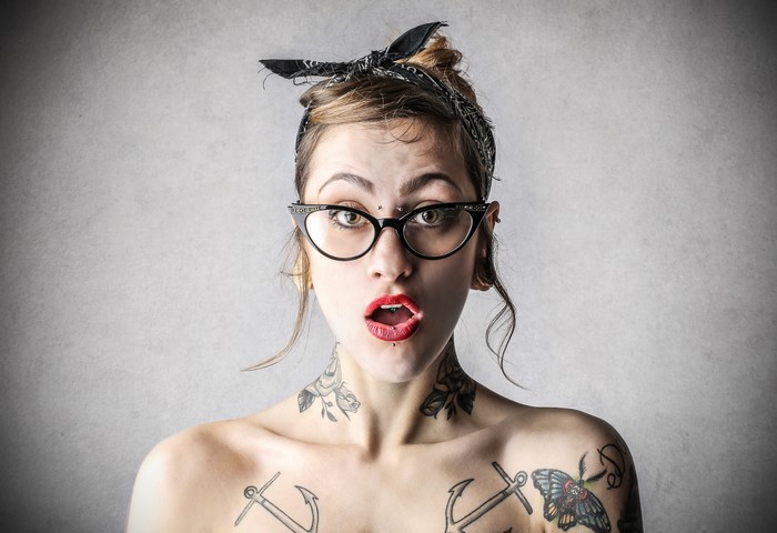 Woman with glasses and tattoos showing surprise