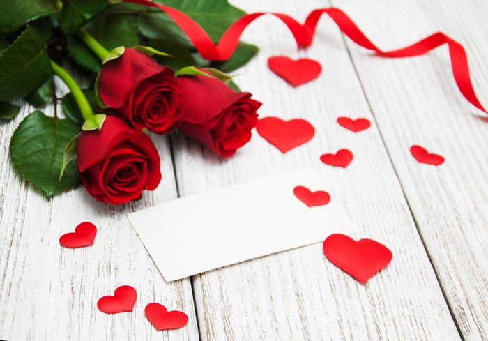 Red roses with ribbon and hearts on wood