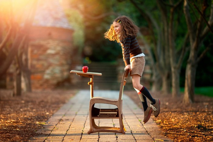 Girl jumping on a school desk with an apple