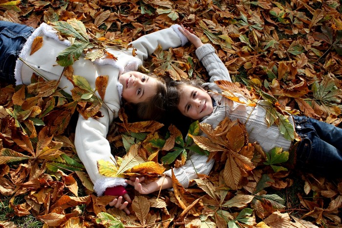 Two young girls lying in autumn foliage