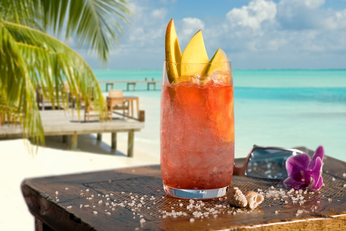Cocktail with mango slices on a beach table