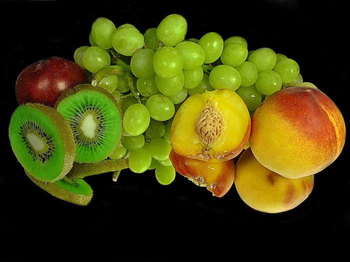 Still life of peaches, kiwi, grapes, and apple on black background with reflection
