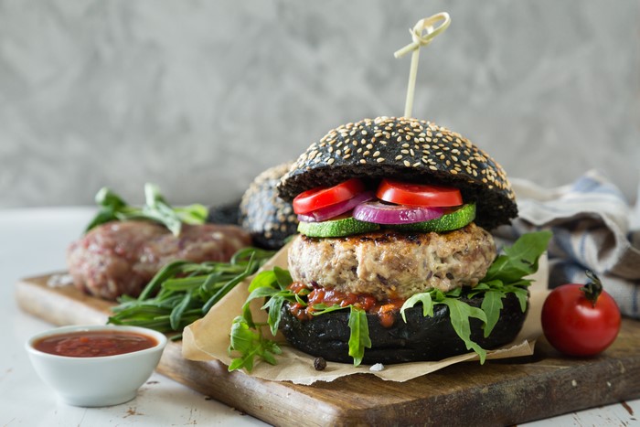 Black sesame bun burger with vegetables on cutting board